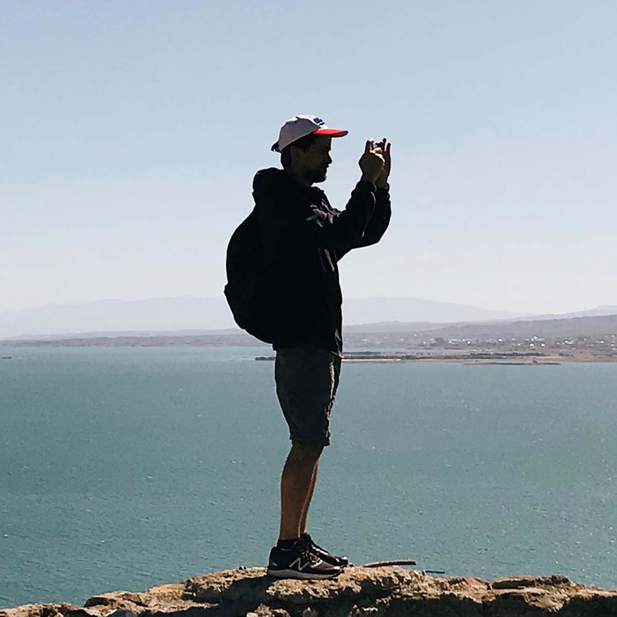A tourist in a cap taking a photo of Lake Sevan